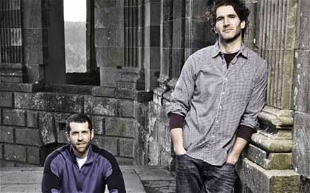 D.B. Weiss sits and David Benioff stands to take a photo.